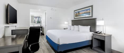 A hotel room with a bed, desk, chair, and a TV.