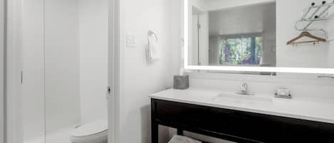 A modern bathroom with a glass shower enclosure, a white toilet, a vanity with a mirror, and a towel rack.