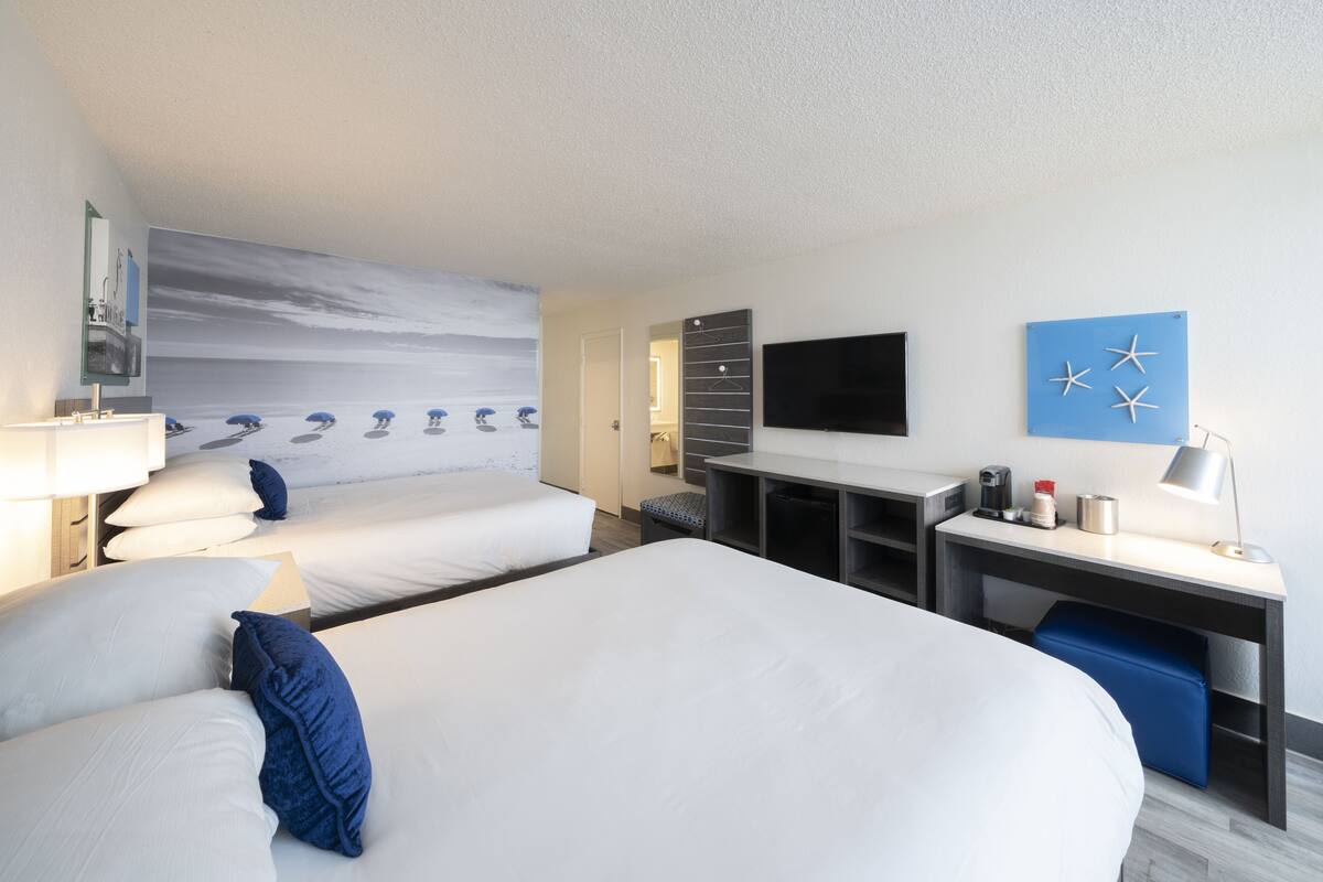 A hotel room with two beds, a desk, a TV, and a wall art piece.