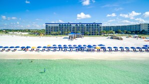 A beach resort with a large building, clear turquoise water, and rows of blue and yellow umbrellas. - The Island Resort at Fort Walton Beach (Fort Walton Beach)