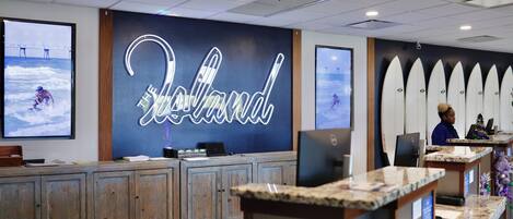 A reception area with a neon sign, surfboards, and a wooden desk.