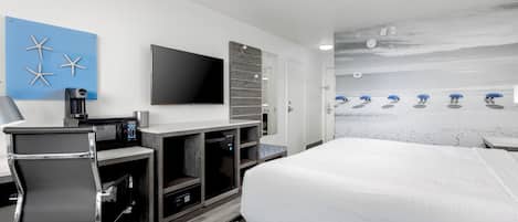 A hotel room with a bed, a desk with a chair, a flat-screen TV, a coffee machine, and a wall-mounted TV.