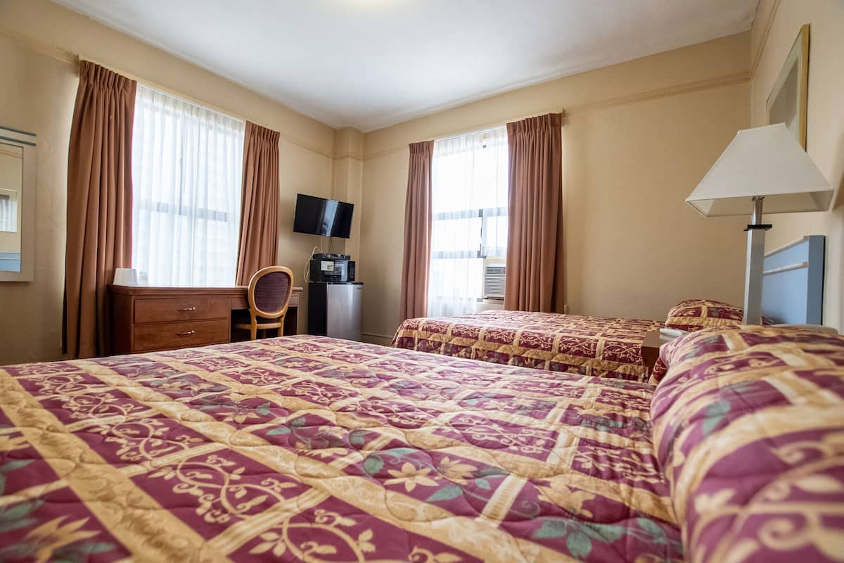 Une chambre d’hôtel avec un grand lit, deux petits lits, un bureau avec une télévision et une chaise.