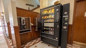 A hotel lobby with a vending machine, a payphone, and a wooden reception desk.