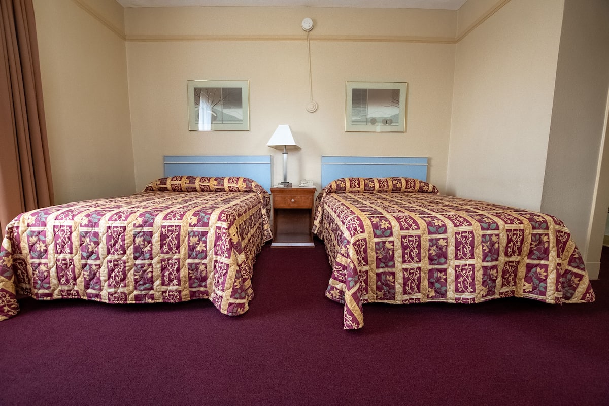 Une chambre d’hôtel avec deux lits, une table de chevet, une lampe et deux tableaux encadrés au mur.