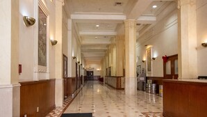 A long, well-lit hallway with marble floors, wooden paneling, and columns.