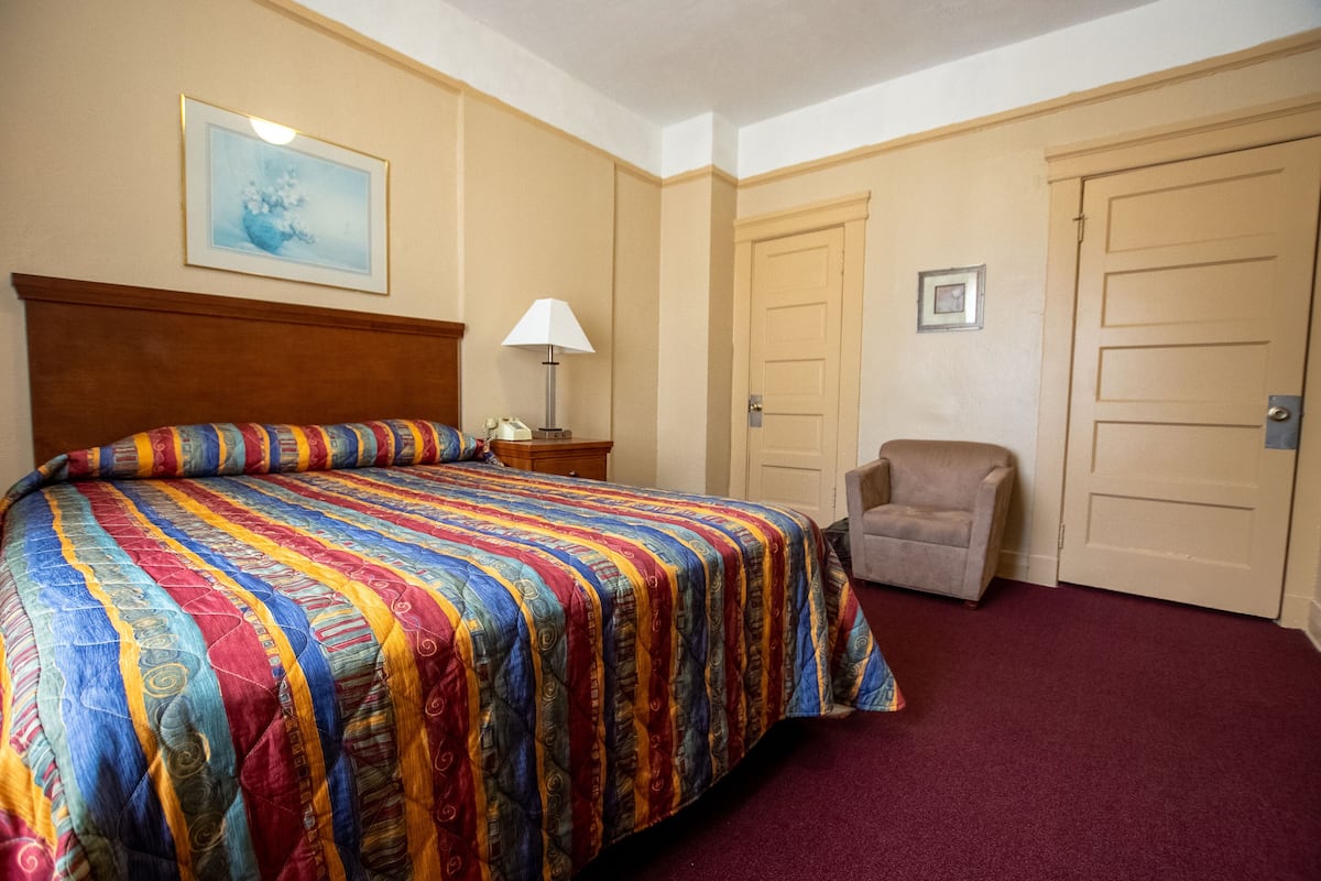 Une chambre d’hôtel avec un grand lit, une chaise, une table de chevet et deux portes.