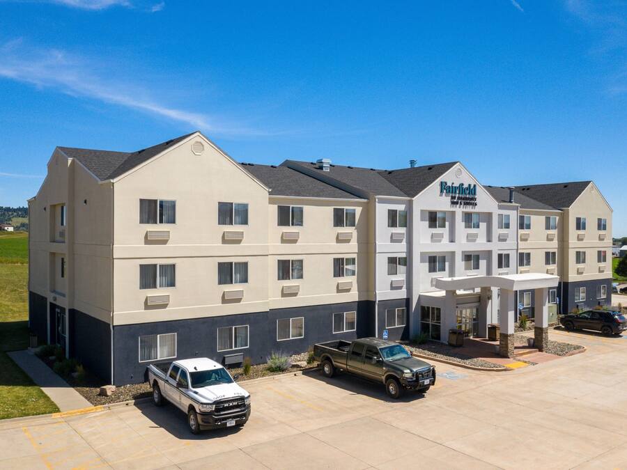 A multi-story hotel with a flat roof, a covered entrance, and a parking lot with several vehicles.