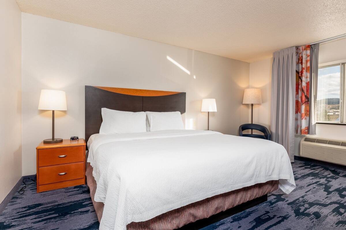 A hotel room with a bed, two bedside tables with lamps, a chair, and a window with curtains.