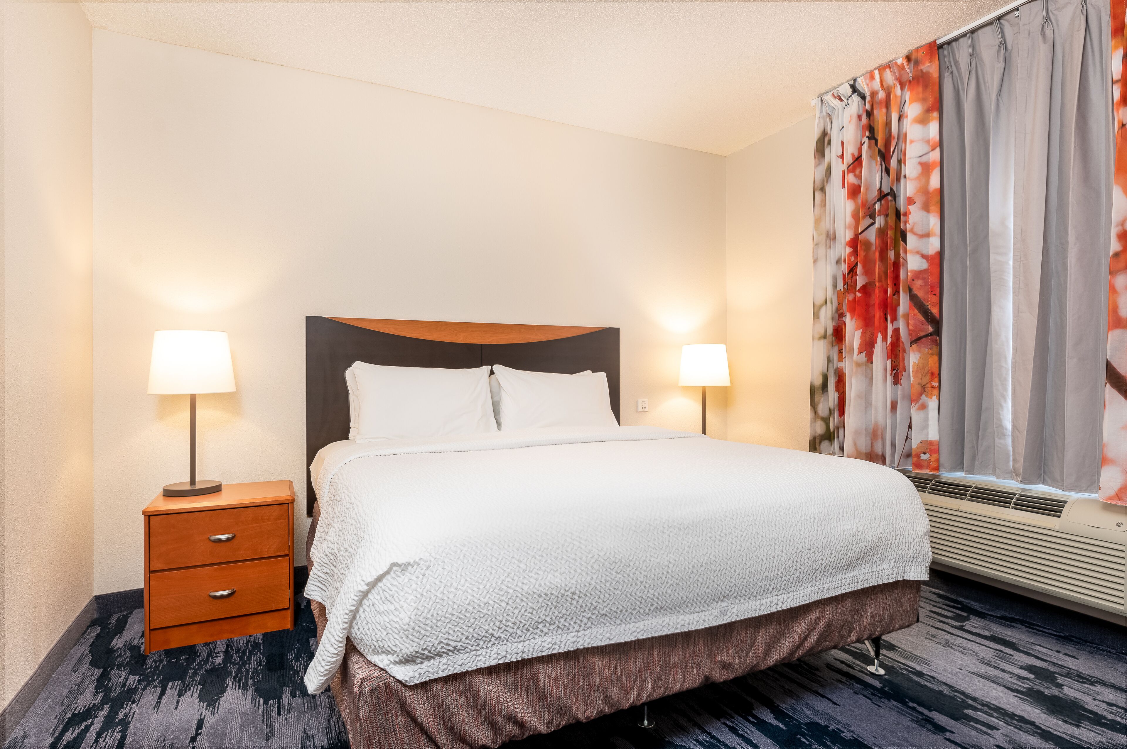 Una habitación de hotel con cama, dos lámparas de noche, una mesita de noche y una ventana con cortinas.