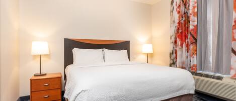 A hotel room with a bed, two bedside lamps, a nightstand, and a window with curtains.