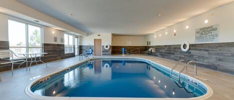 Une piscine intérieure à l’eau claire, avec un panneau indiquant la présence d’un sauveteur et une vue sur l’extérieur grâce à de grandes fenêtres.