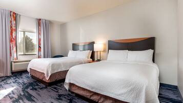 A hotel room with two beds, a window with curtains, a wall-mounted lamp, and a carpeted floor.