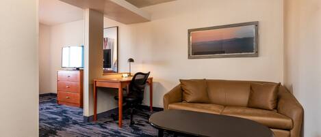 Une chambre d’hôtel avec un canapé en cuir marron, une petite table, un bureau avec une chaise et un tableau encadré au mur.