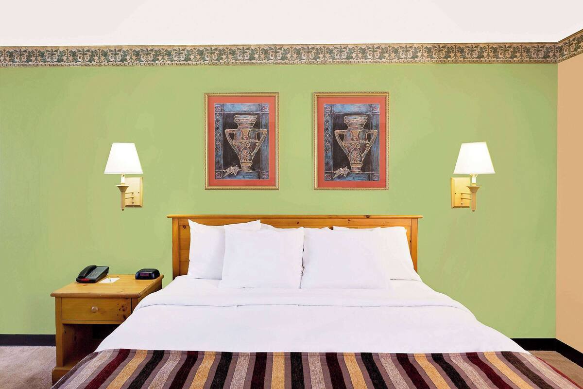 A hotel room with a bed, two wall-mounted lamps, a nightstand with a phone, and two framed pictures on the wall.