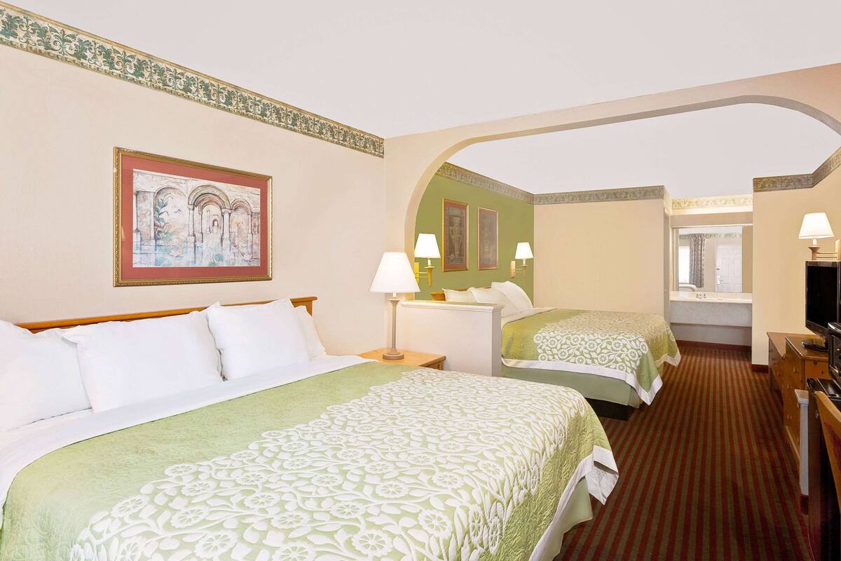 A hotel room with two beds, a television, a desk, and a window.