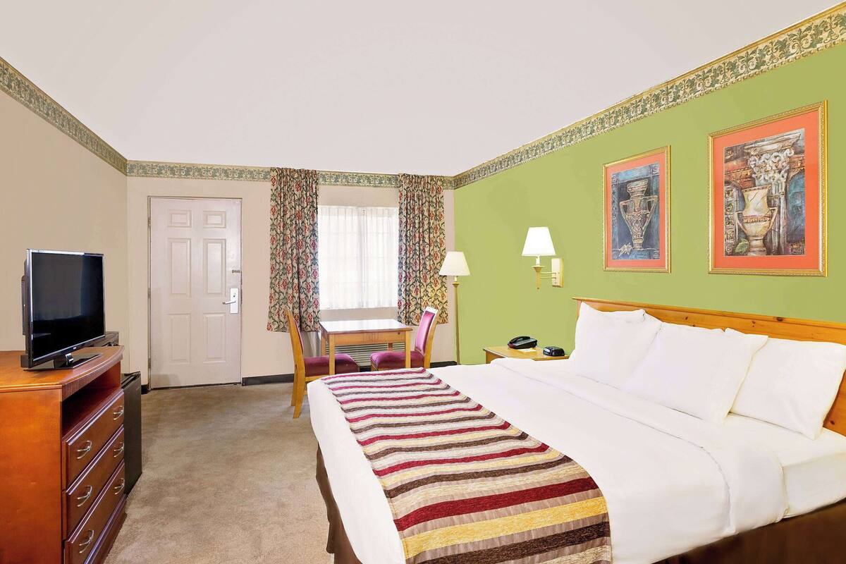 A hotel room with a bed, a desk, a chair, a television, and a lamp.
