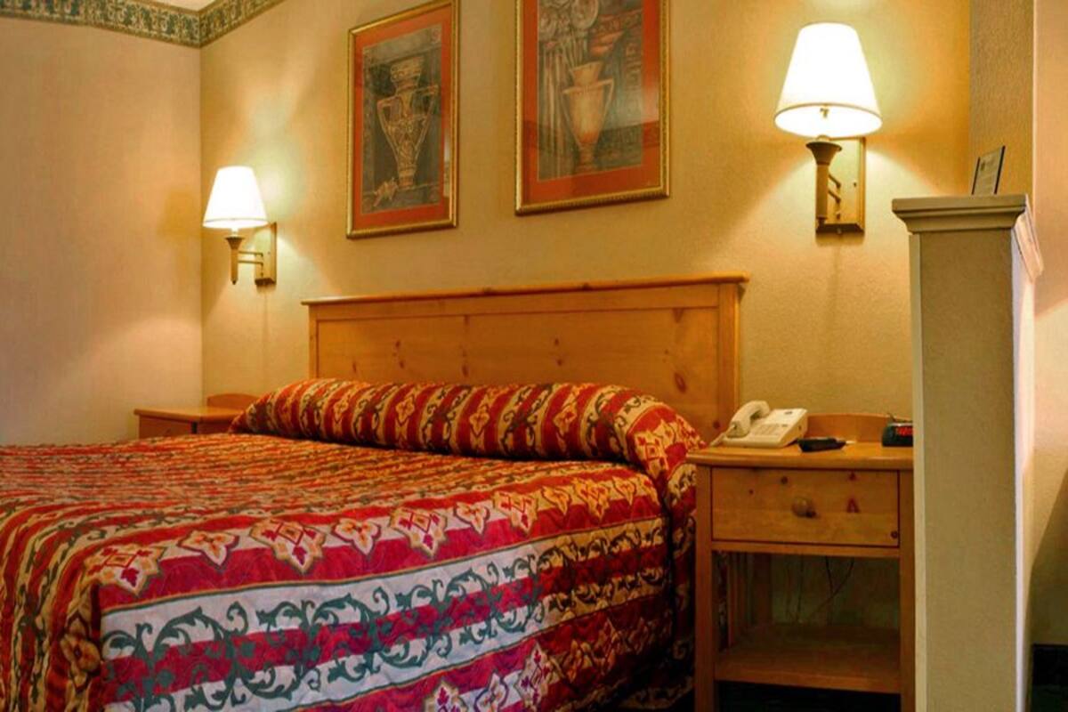A hotel room with a wooden headboard, a bed with a patterned bedspread, two wall-mounted lamps, a bedside table with a phone, and a nightstand.