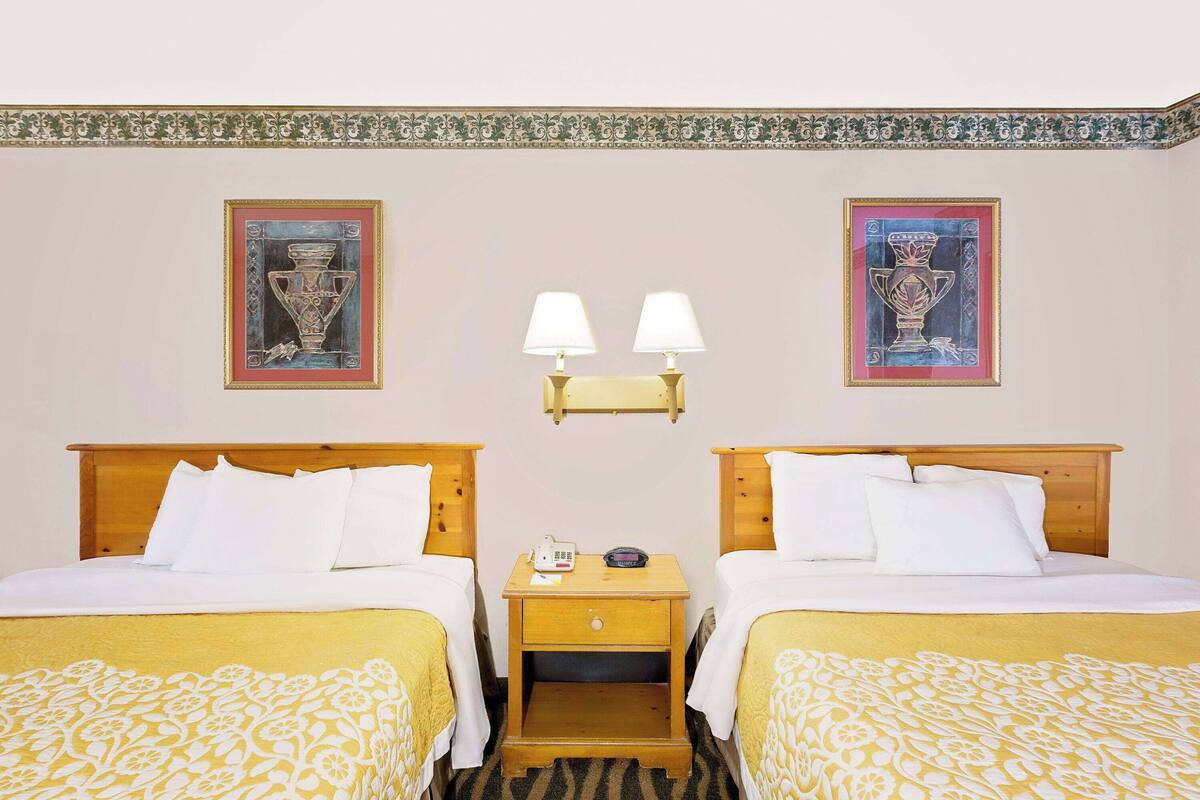 A hotel room with two single beds, a nightstand with a lamp, and two framed pictures on the wall.