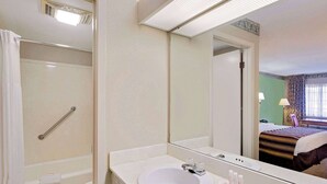 Casa de banho com lavatório branco, espelho e chuveiro.