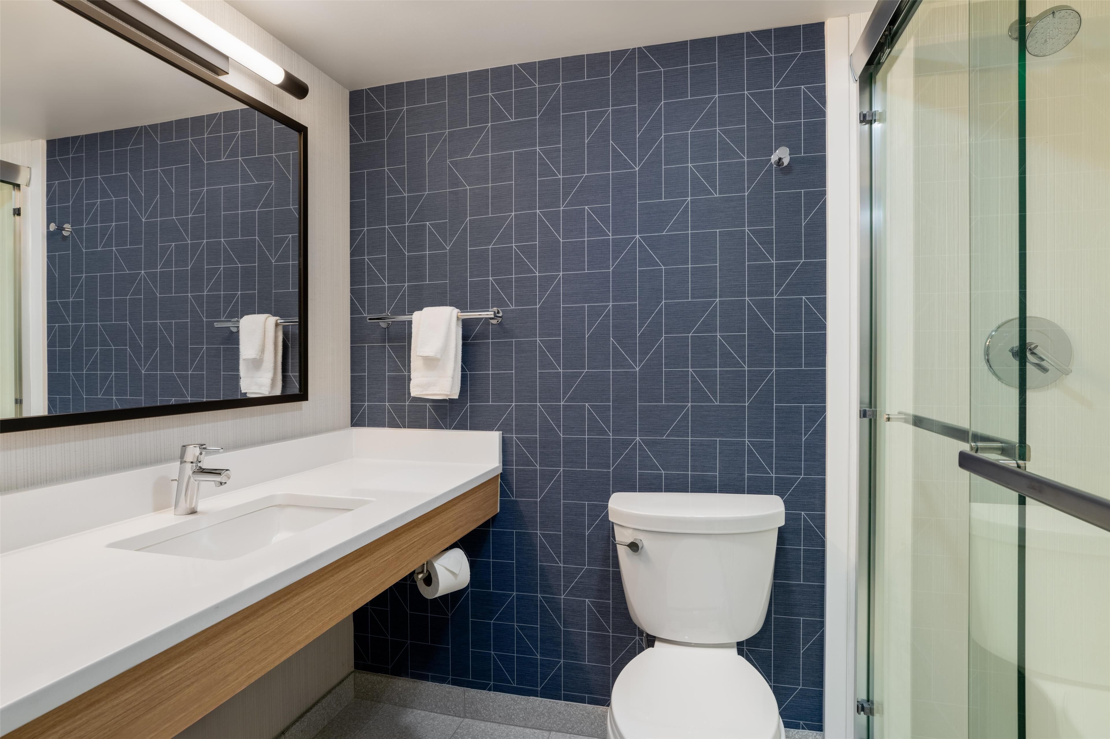 Un baño moderno con lavamanos blanco, un espejo, inodoro y cabina de ducha de vidrio.