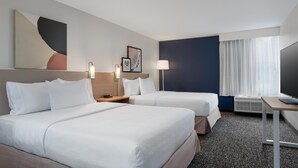 A hotel room with two beds, a desk, a television, and a large window with curtains.