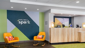A hotel reception area with two rocking chairs, a wooden reception desk, and a wall with a geometric design and the text "It only takes a spark".