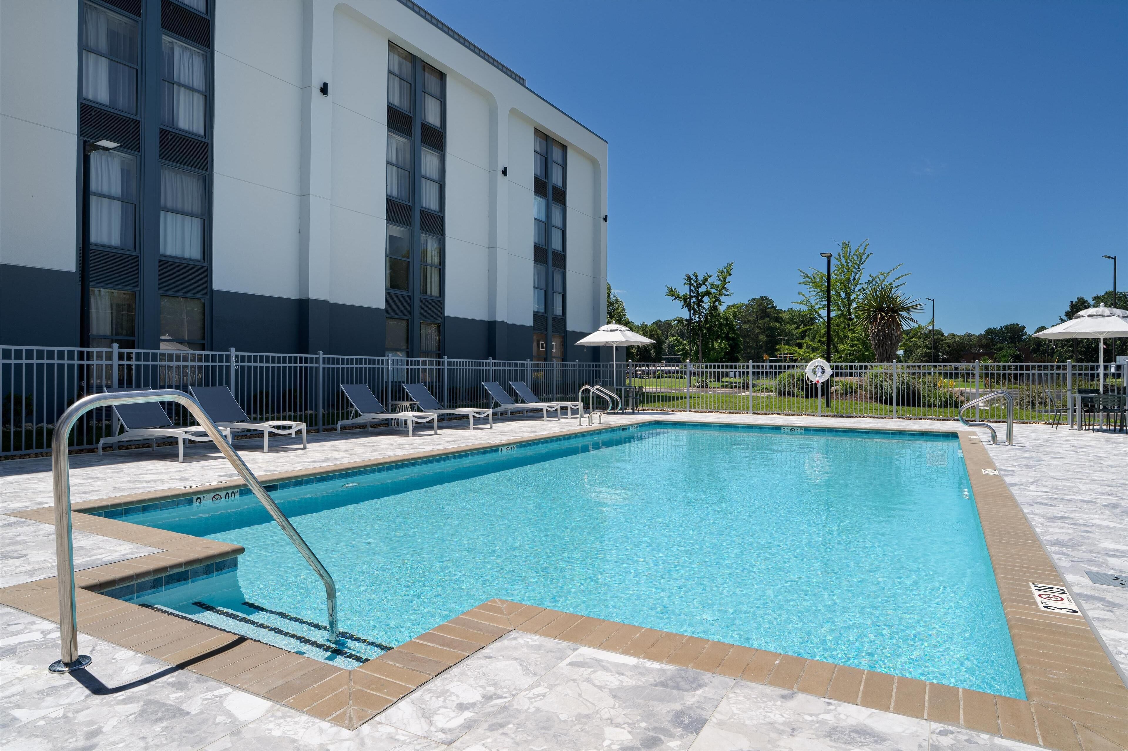 A rectangular swimming pool with a metal ladder, surrounded by a tiled deck.