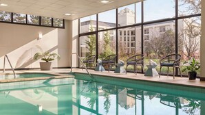 Une piscine intérieure avec des parois en verre transparent, des plantes en pot et une vue sur les bâtiments et les arbres à l’extérieur.