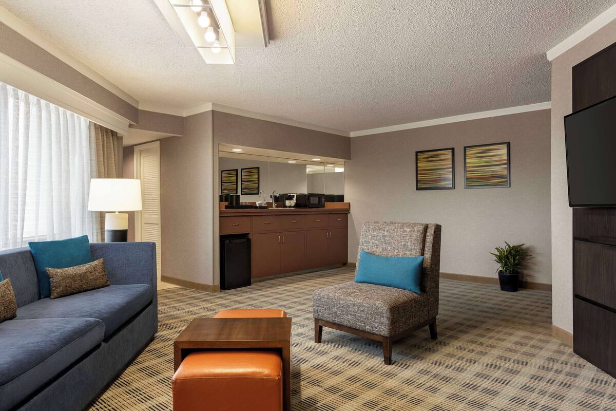 Ein Hotelzimmer mit Sofa, Sessel, Hocker, Küchenzeile und einem großen Spiegel.