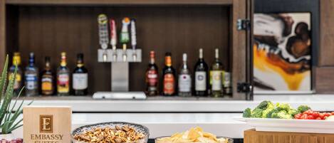 A bar area with a variety of liquor bottles and a buffet with assorted cheeses, fruits, and vegetables.