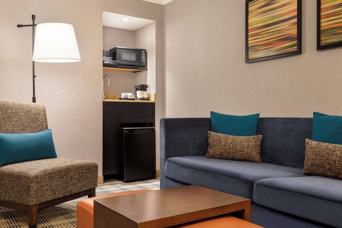 Ein Hotelzimmer mit Sofa, Sessel, Kaffeemaschine, Mikrowelle und einem Kunstwerk an der Wand.