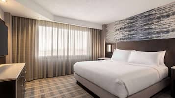 A hotel room with a large bed, a desk, and a large window with curtains.