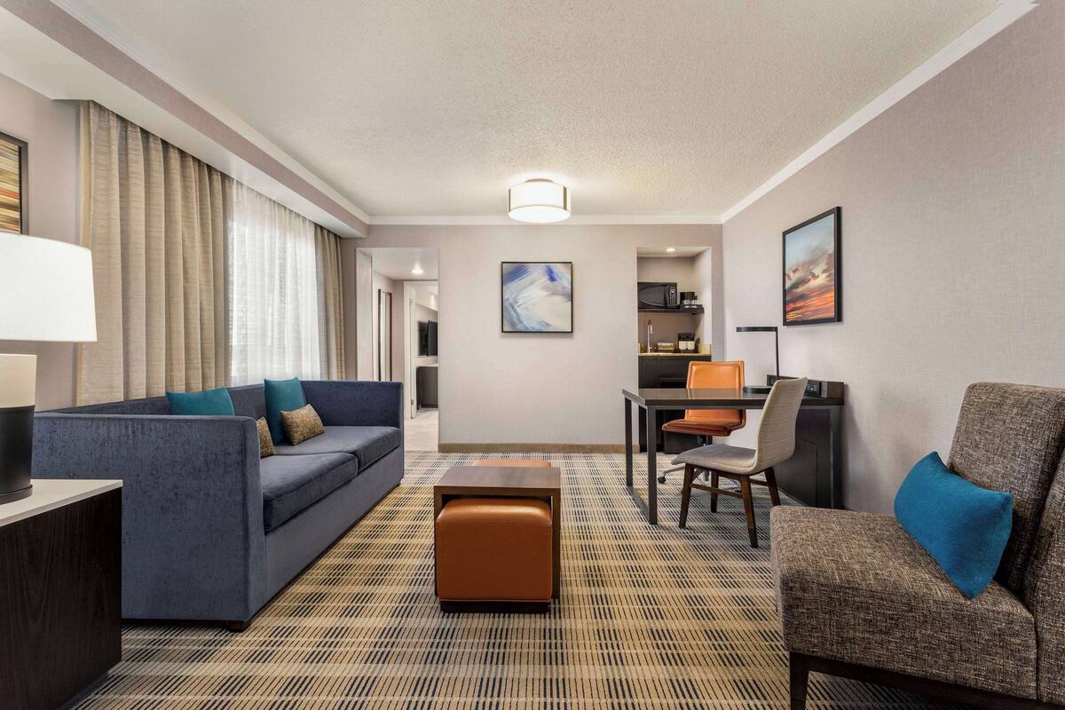 Ein Hotelzimmer mit Sofa, Sessel, Hocker, Esstisch und einer Küchenzeile.