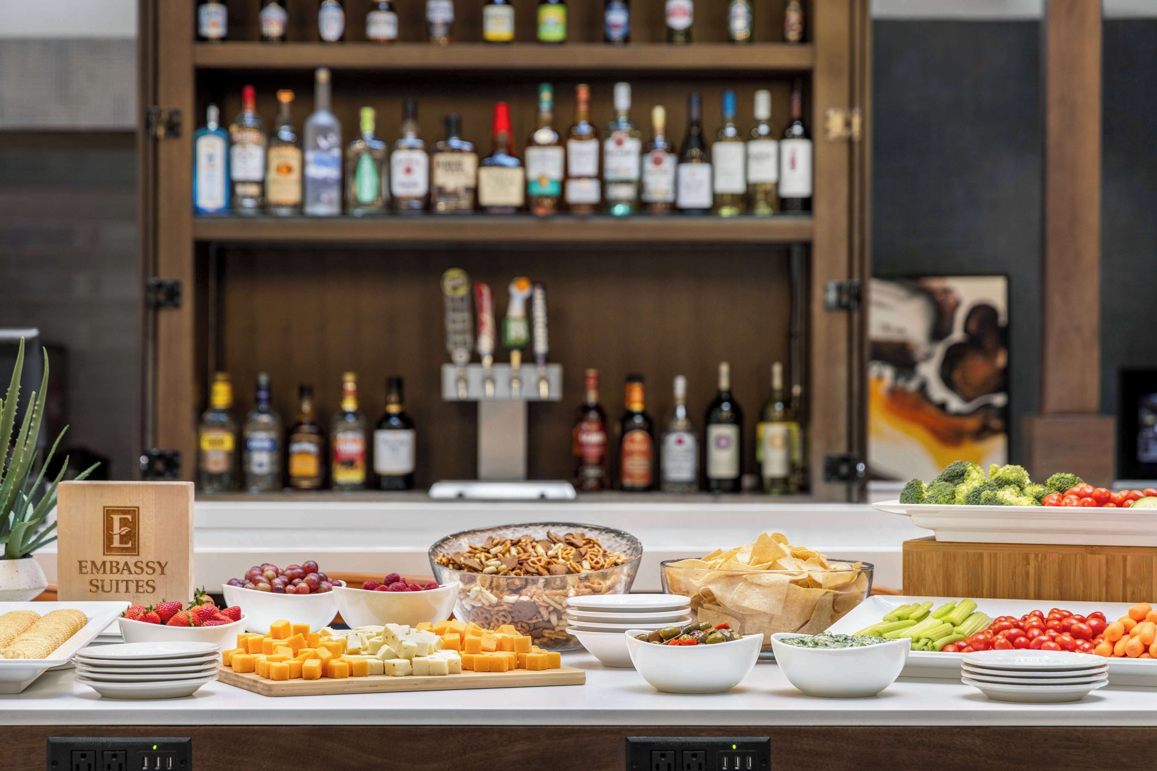 A buffet table with various food items and a bar with multiple liquor bottles in the background.