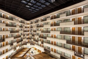 Interior de un hotel de varios pisos con un atrio central, balcones y una escalera.