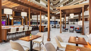 Un hall d’hôtel moderne doté d’un bar, d’espaces aménagés avec des sièges et d’un escalier reliant plusieurs étages.