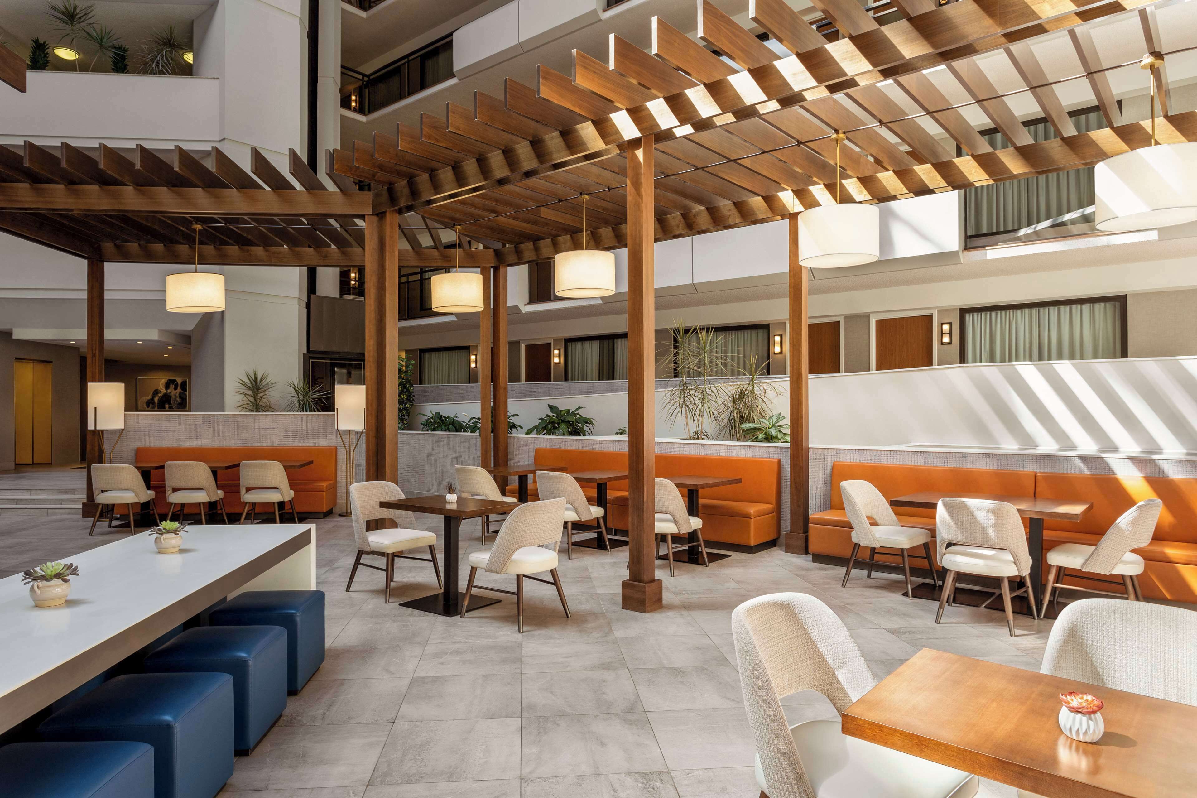 Un espacio interior moderno con varias zonas de estar, incluidas mesas y sofás, bajo una pérgola de madera.
