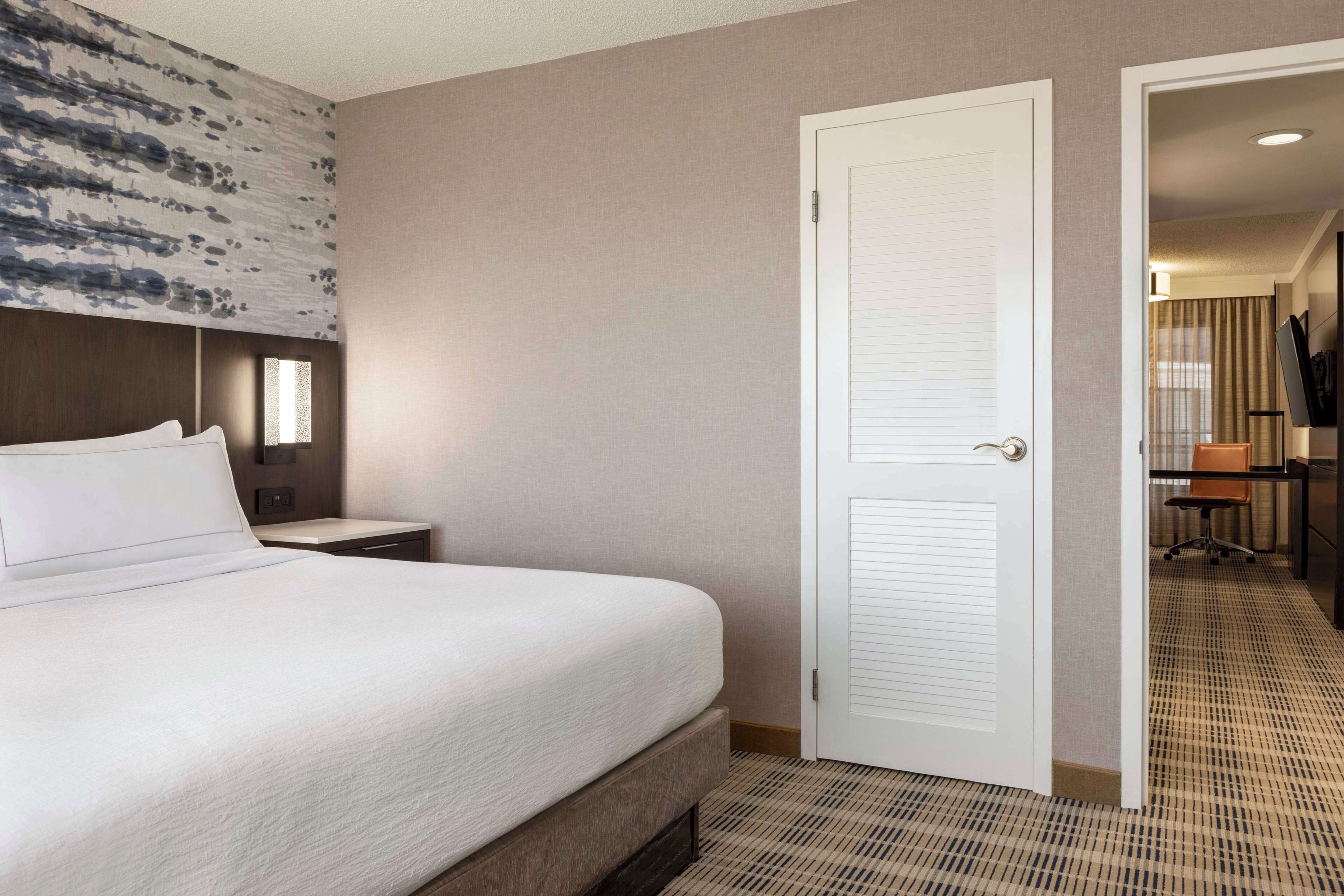 A hotel room with a large bed, a bedside table, a wardrobe, and a door leading to a bathroom.