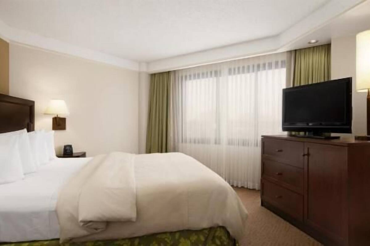Ein Hotelzimmer mit Bett, Fernseher auf einer Kommode und einem fenster mit Vorhängen.