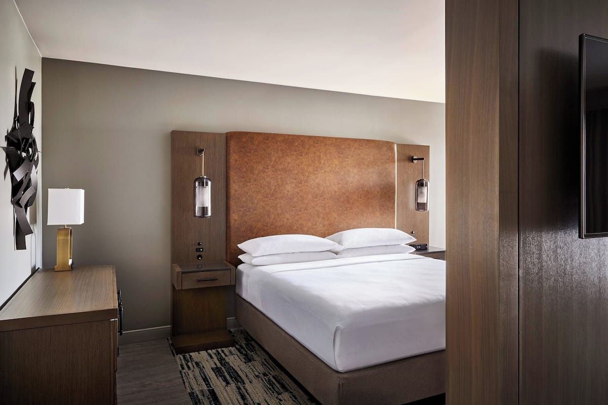 Une chambre d’hôtel moderne avec une tête de lit en bois, une table de chevet avec une lampe et un téléviseur à écran plat fixé au mur.