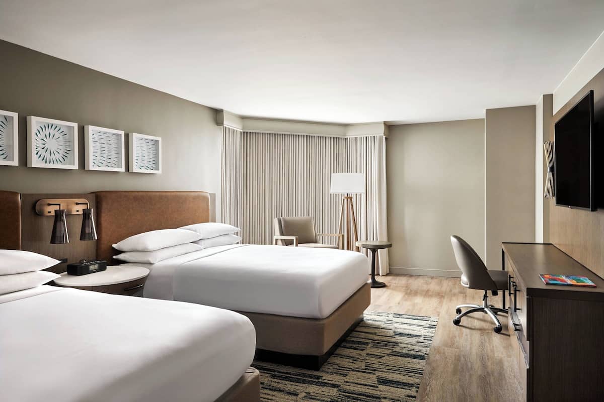 Une chambre d’hôtel avec deux lits, un bureau, une chaise, une télévision et une fenêtre avec des rideaux.