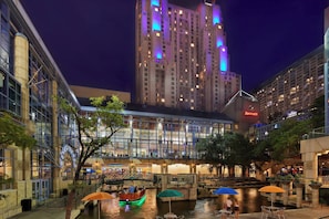A nighttime view of a hotel with a river, a bridge, and outdoor seating areas. - San Antonio Marriott Rivercenter on the River Walk (San Antonio)