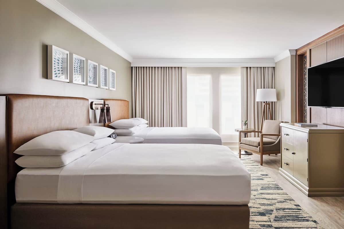 Une chambre d’hôtel avec deux lits, un bureau, une télévision et une grande fenêtre avec des rideaux.