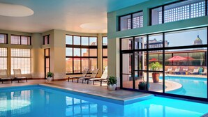 Piscina interior con sillones de descanso y amplias ventanas con vistas a la ciudad.