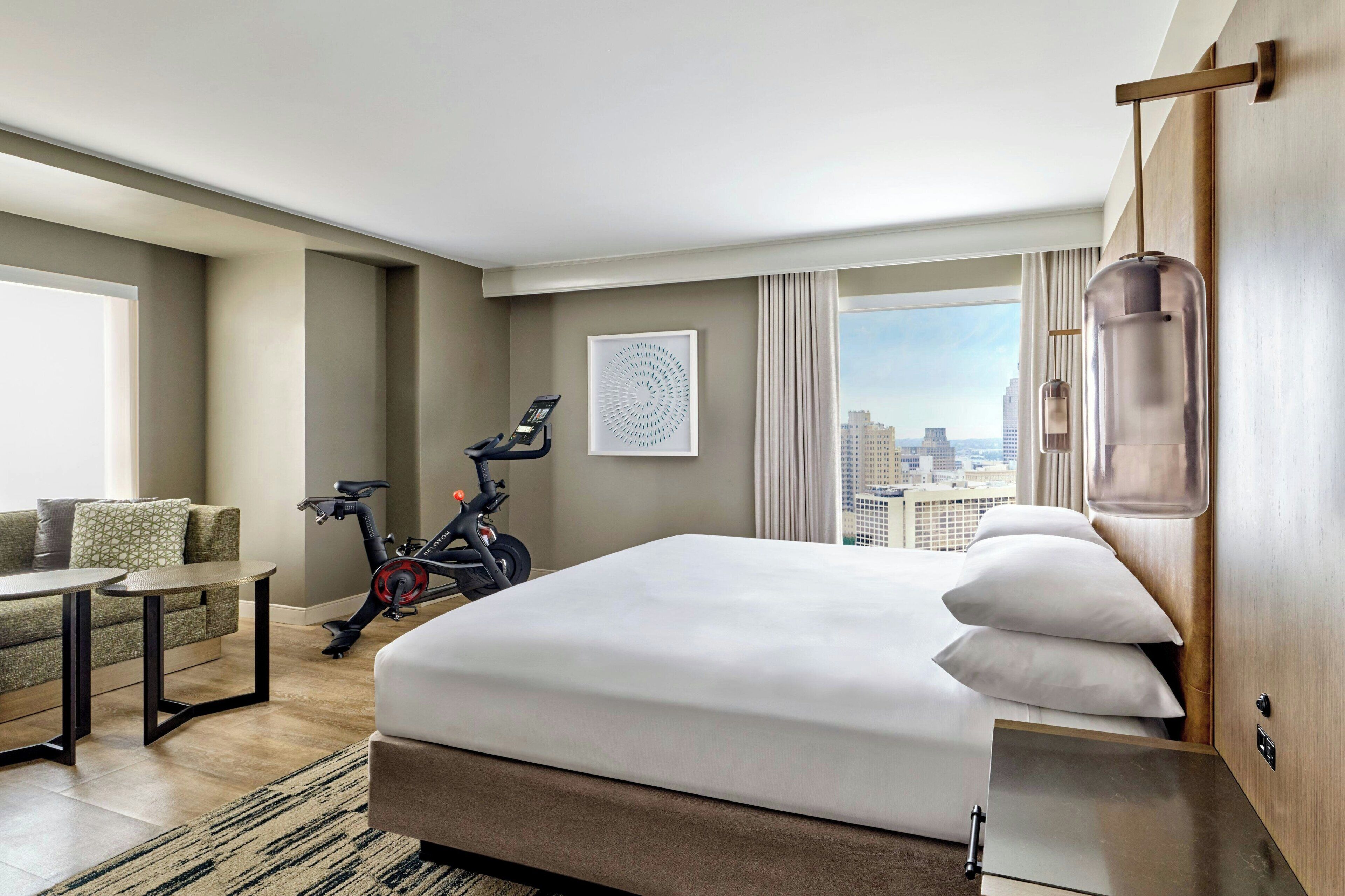 Une chambre d’hôtel avec un lit, un bureau, un vélo d’exercice et une vue sur la ville.