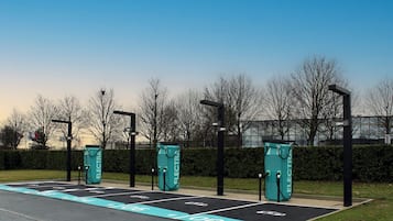 An electric vehicle charging station with three charging points, a clear sky, and leafless trees in the background.