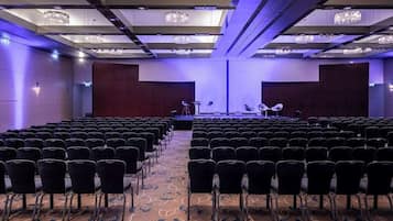 A conference room with rows of chairs, a stage with a podium, and chandeliers.