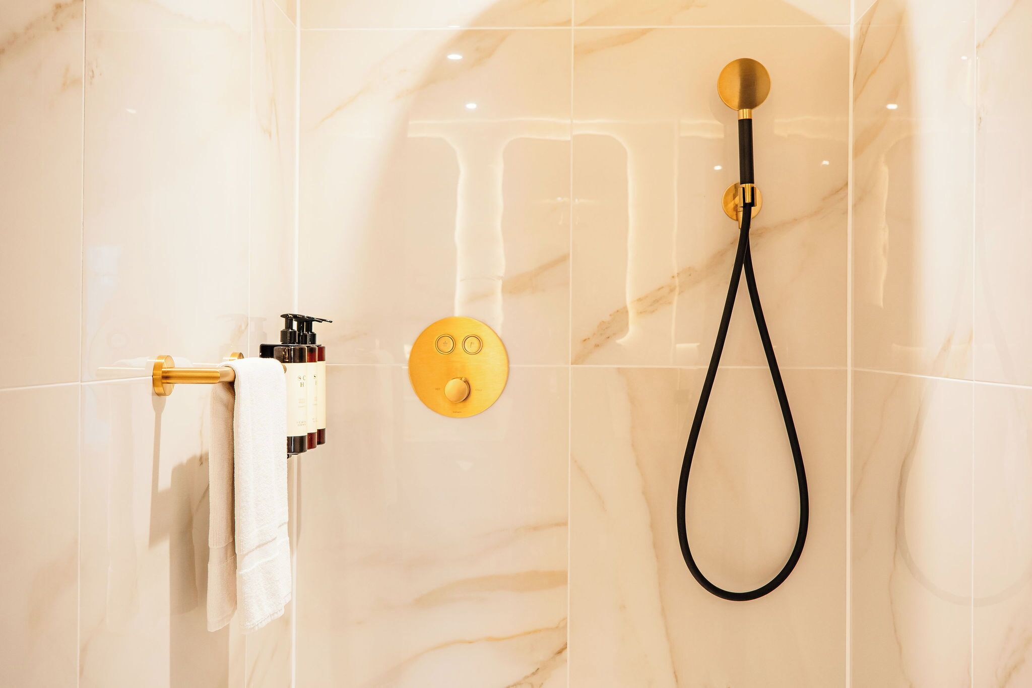 A modern bathroom with a marble wall, a gold showerhead, and a towel rack with a white towel.