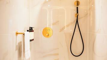 A modern bathroom with a marble wall, a gold showerhead, and a towel rack with a white towel.